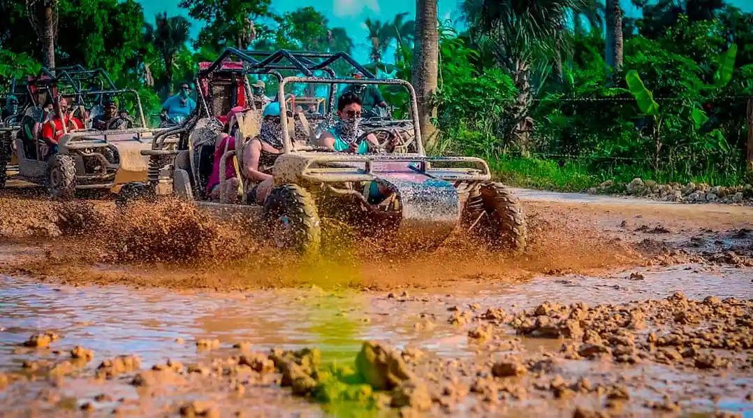 A group of travelers driving ATVs and buggies splashing through mud puddles on the Full Dominican Adventure tour.