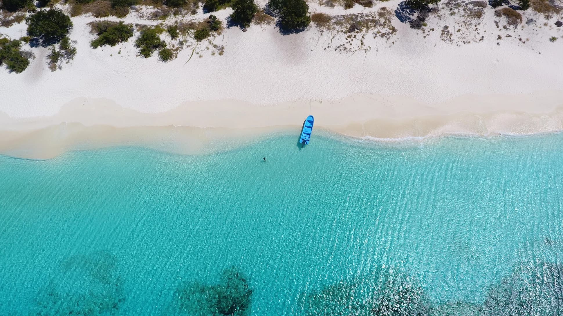 Aerial view of Bahía de las Águilas coastline with turquoise Caribbean waters, white sand, and a small blue boat anchored on the shore.